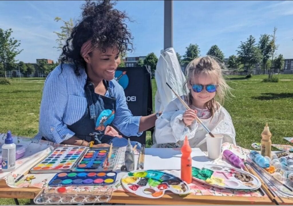Ailyne Stein, oprichter van De Bloeiboei, schildert buiten met een kind aan tafel aan knutselprojecten.