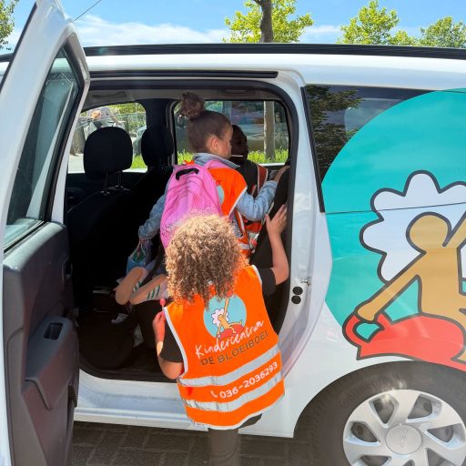Twee kinderen dragen oranje hesjes met het logo van Kindercentrum De Bloeiboei terwijl ze de auto instappen.
