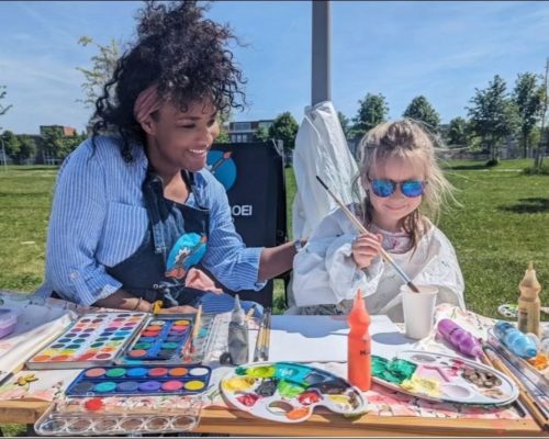 Ailyne Stein, oprichter van De Bloeiboei, schildert buiten met een kind aan tafel aan knutselprojecten.