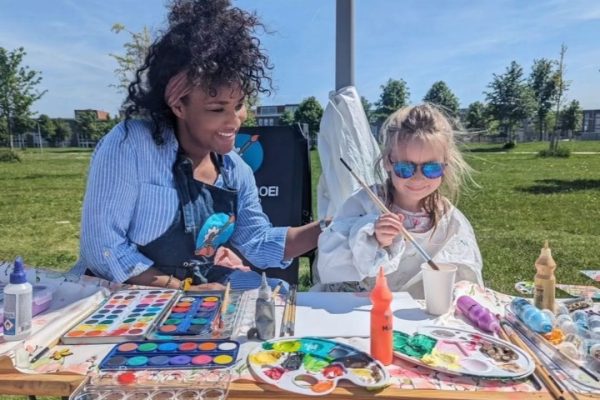 Ailyne Stein, oprichter van De Bloeiboei, schildert buiten met een kind aan tafel aan knutselprojecten.