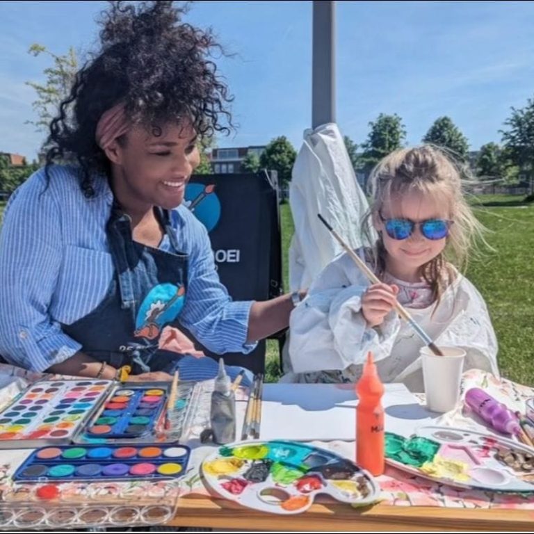 Ailyne Stein, oprichter van De Bloeiboei, schildert buiten met een kind aan tafel aan knutselprojecten.