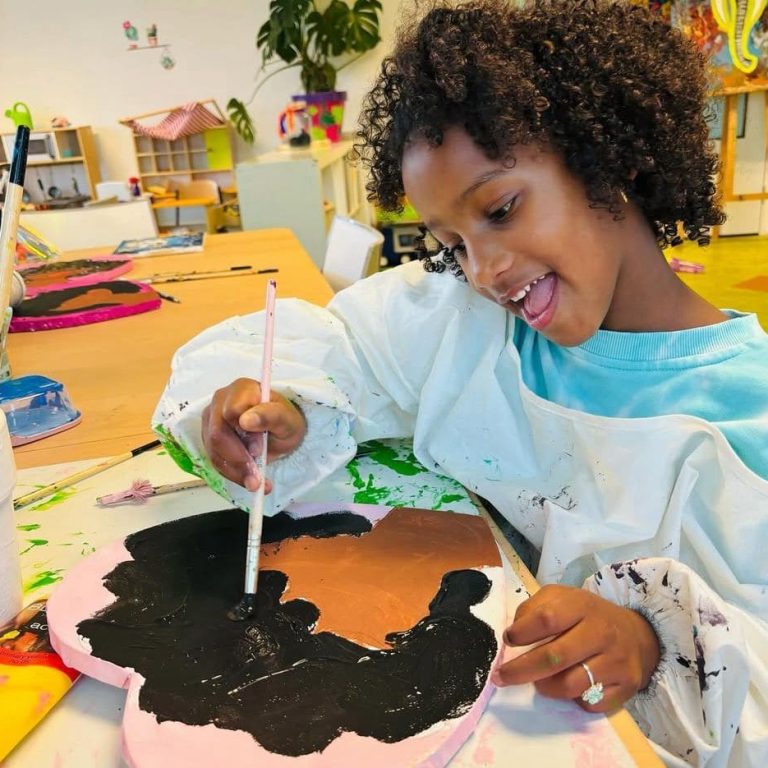 Een lachend meisje werkt aan een schilderopdracht in Kindercentrum De Bloeiboei.